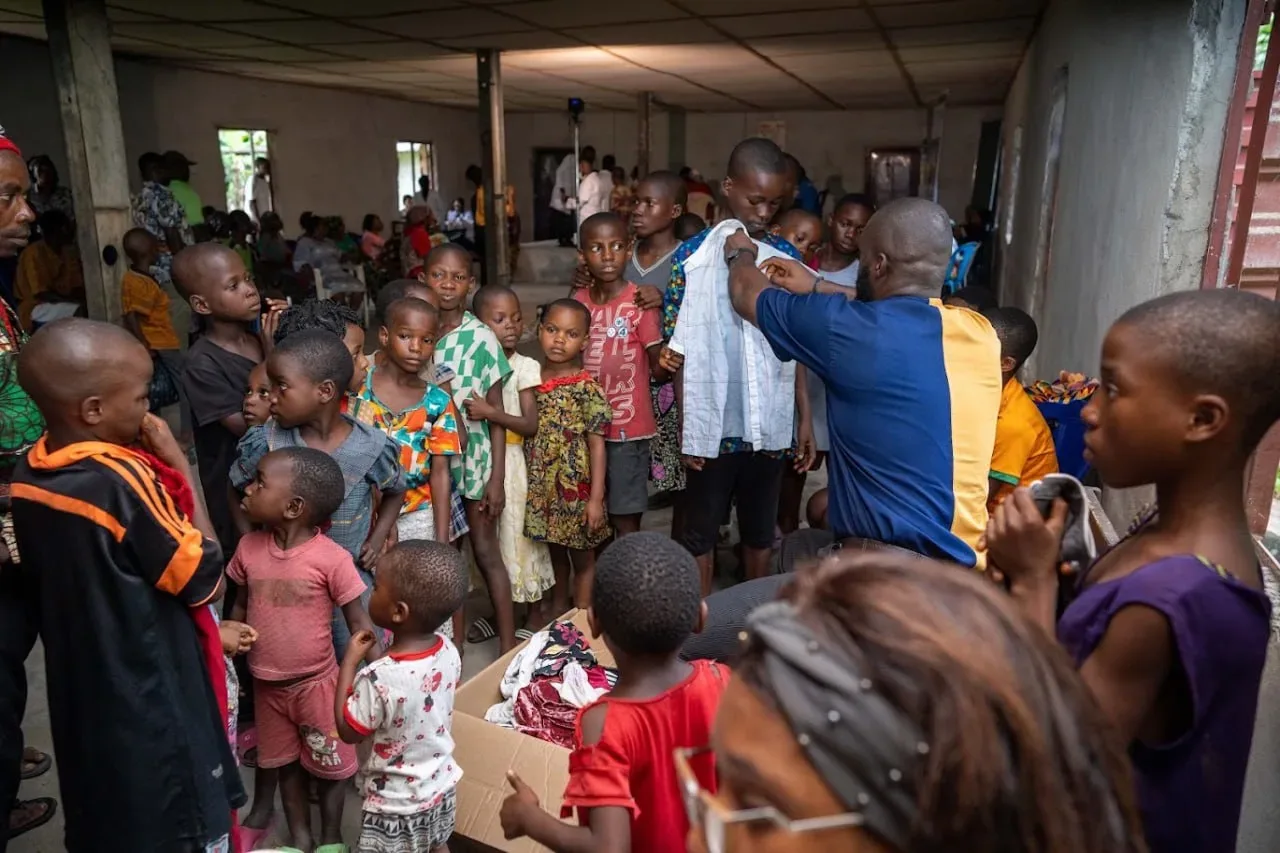 A GAMAID volunteer checks a shirt for size against a boy as children wait their turn